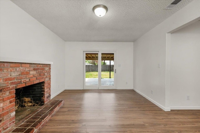 unfurnished living room featuring a textured ceiling, a brick fireplace, wood finished floors, and visible vents