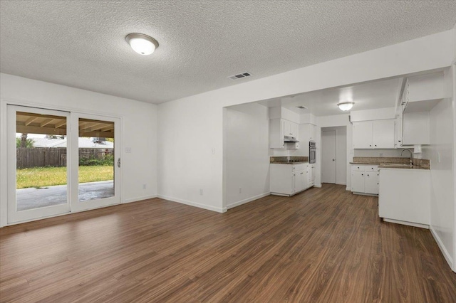 unfurnished living room with a sink, a textured ceiling, dark wood finished floors, baseboards, and visible vents