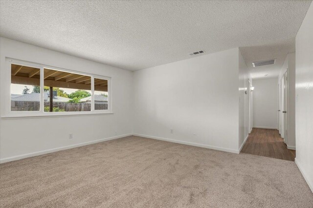empty room with visible vents, carpet flooring, baseboards, and a textured ceiling