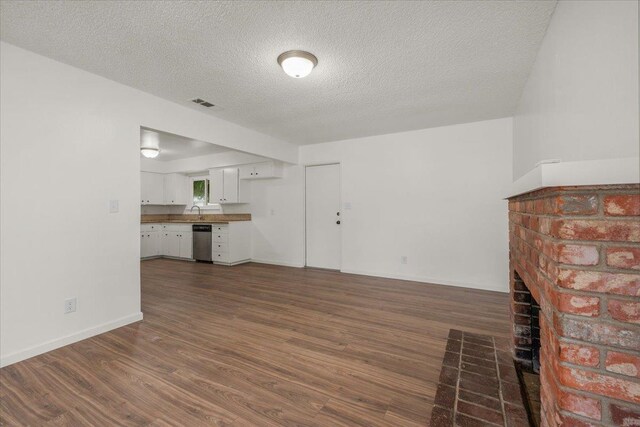 unfurnished living room featuring a textured ceiling, visible vents, a brick fireplace, dark wood finished floors, and baseboards