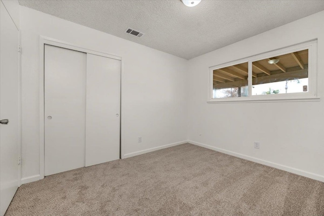 unfurnished bedroom featuring a textured ceiling, visible vents, carpet floors, baseboards, and a closet