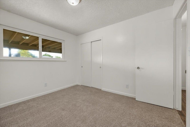 unfurnished bedroom with carpet floors, a textured ceiling, baseboards, and a closet
