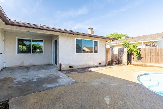 back of house featuring crawl space, a chimney, a patio, and stucco siding