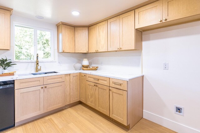 kitchen featuring light brown cabinetry, a sink, dishwasher, light wood-style flooring, and baseboards
