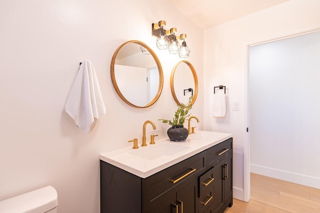 bathroom with double vanity, wood finished floors, toilet, baseboards, and a sink