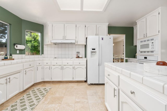 kitchen featuring white appliances, tile counters, white cabinetry, under cabinet range hood, and tasteful backsplash