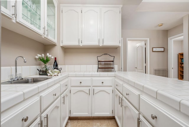 kitchen featuring a sink, light tile patterned floors, glass insert cabinets, tile counters, and white cabinetry