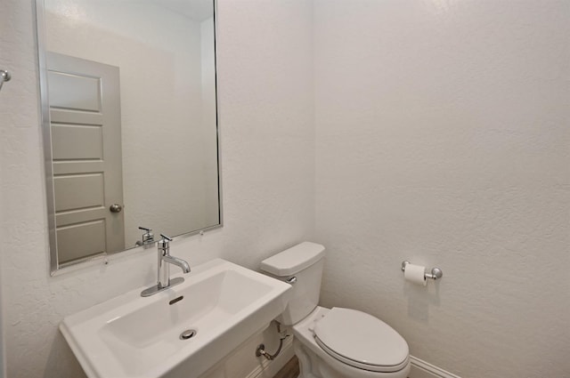 half bath featuring toilet, a sink, and a textured wall
