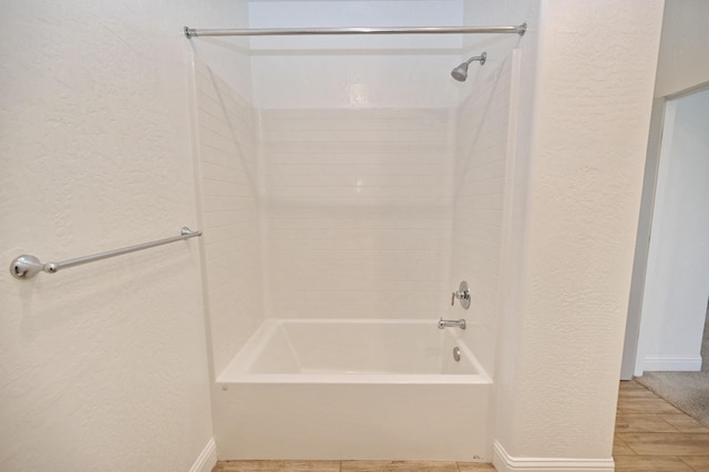 bathroom with baseboards, shower / tub combination, and a textured wall