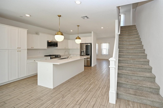 kitchen featuring appliances with stainless steel finishes, light wood finished floors, visible vents, light countertops, and an island with sink