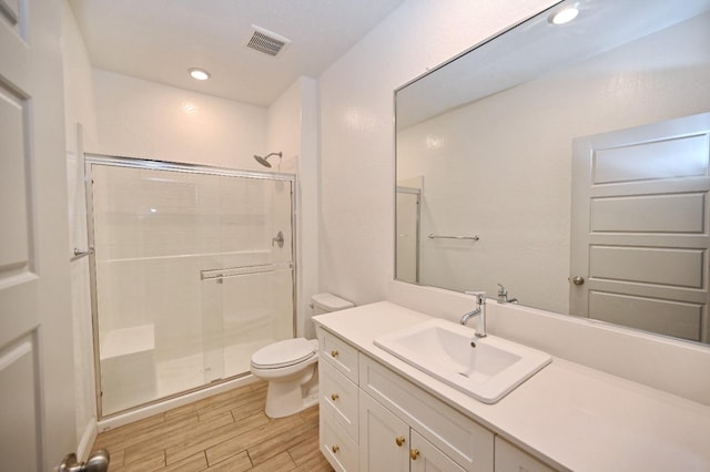 bathroom featuring toilet, wood finished floors, vanity, visible vents, and a stall shower