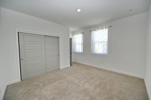 unfurnished bedroom with a closet, light carpet, and baseboards