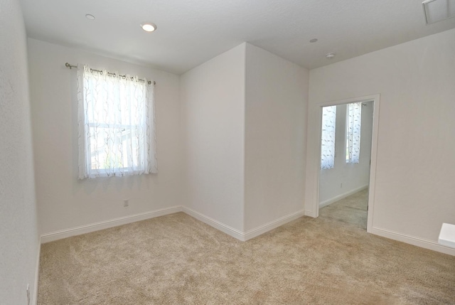 empty room with plenty of natural light, light carpet, baseboards, and visible vents