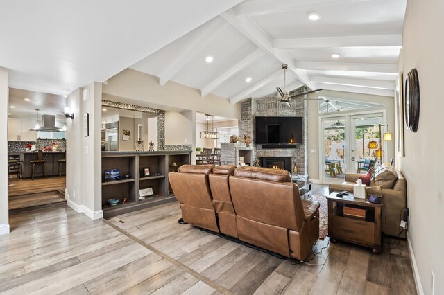 living room with light wood-style floors, baseboards, ceiling fan, a large fireplace, and lofted ceiling with beams
