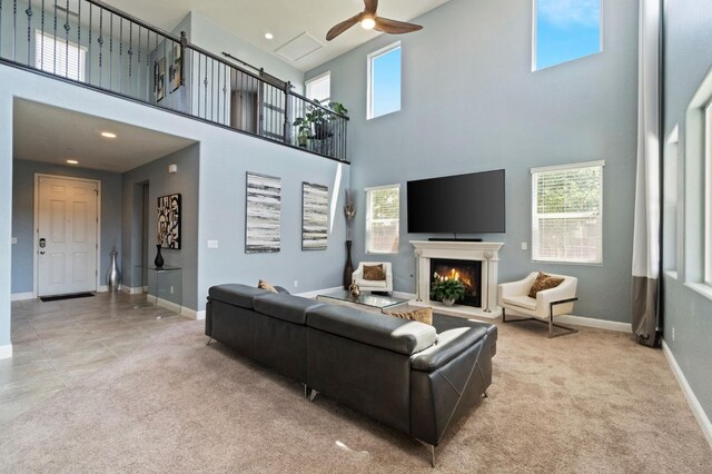 living area featuring carpet flooring, a ceiling fan, a high ceiling, and a warm lit fireplace