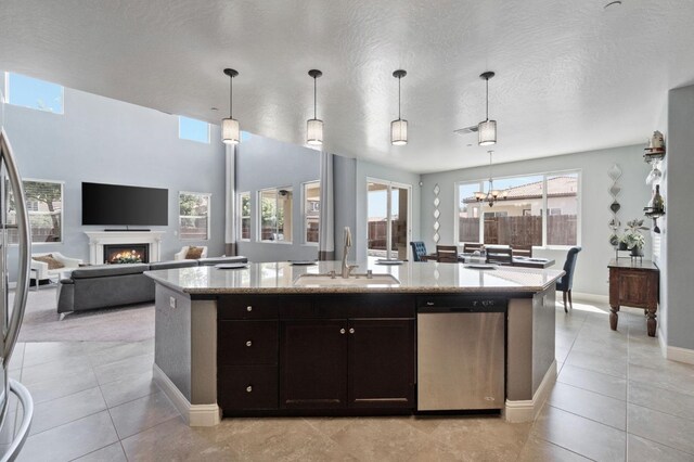 kitchen featuring a warm lit fireplace, appliances with stainless steel finishes, light stone counters, a sink, and an island with sink