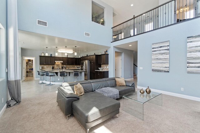 living area featuring baseboards, light colored carpet, a towering ceiling, and visible vents