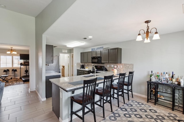 kitchen featuring an inviting chandelier, tasteful backsplash, a sink, light wood-style flooring, and black appliances