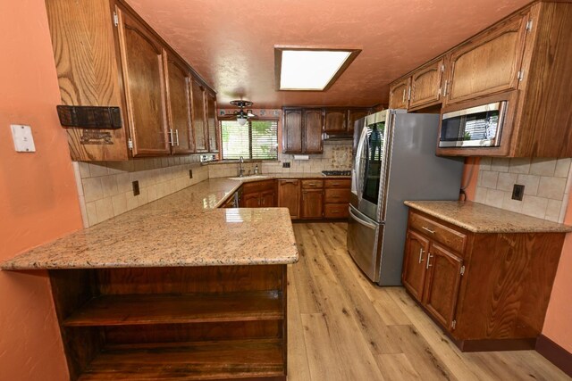 kitchen featuring light stone countertops, a sink, light wood-style floors, stainless steel appliances, and decorative backsplash