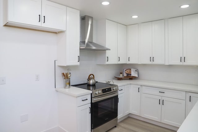 kitchen featuring wall chimney range hood, light countertops, white cabinets, and stainless steel range with electric cooktop