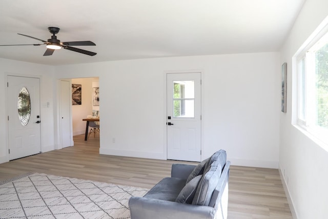 living area featuring baseboards, a ceiling fan, light wood finished floors, and a wealth of natural light