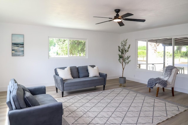 living area with baseboards, a ceiling fan, and light wood-style flooring