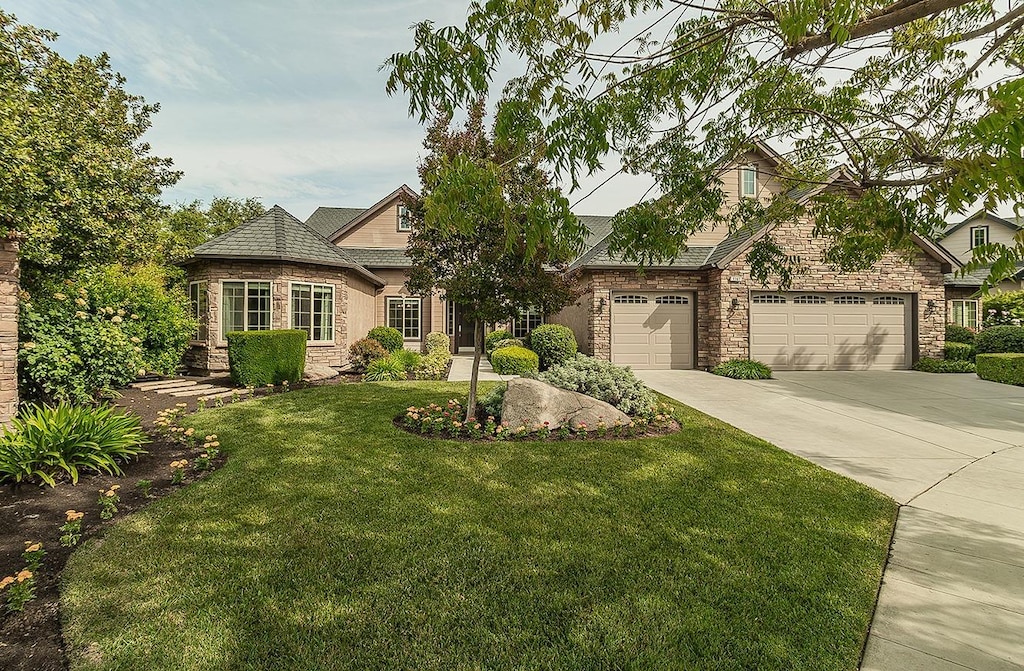 view of front facade featuring a garage, a front yard, stone siding, and concrete driveway