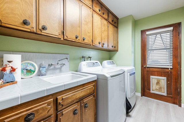 clothes washing area with cabinet space, a sink, baseboards, light wood-type flooring, and washer and clothes dryer