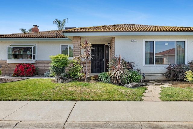 view of front of home with a front lawn, stucco siding, a chimney, brick siding, and a tiled roof