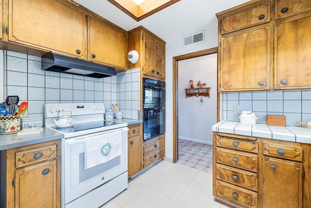 kitchen featuring visible vents, dobule oven black, electric stove, backsplash, and under cabinet range hood
