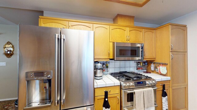 kitchen with light brown cabinetry, decorative backsplash, stainless steel appliances, and tile countertops