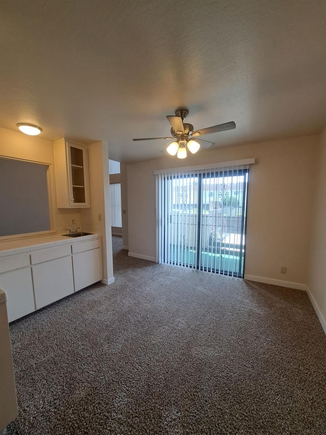 unfurnished living room with a sink, baseboards, a ceiling fan, and carpet floors
