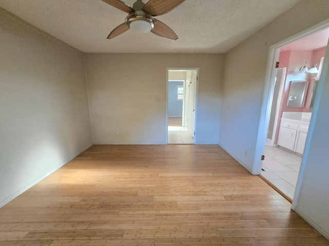 empty room with a ceiling fan, light wood finished floors, and a textured ceiling