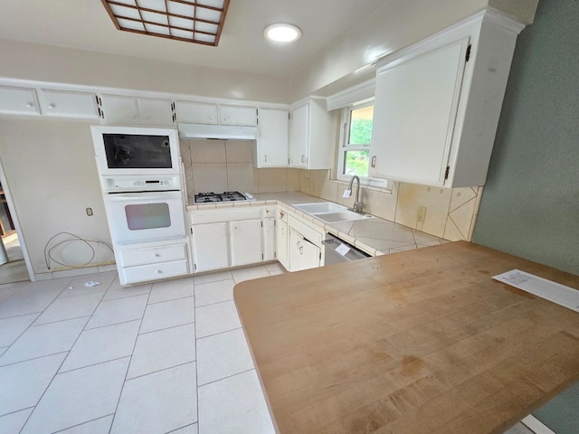 kitchen featuring decorative backsplash, white oven, tile countertops, under cabinet range hood, and a sink