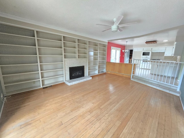 unfurnished living room featuring ornamental molding, a brick fireplace, ceiling fan, light wood-type flooring, and a textured ceiling