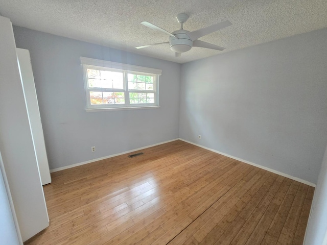 empty room featuring ceiling fan, a textured ceiling, baseboards, light wood-type flooring, and visible vents