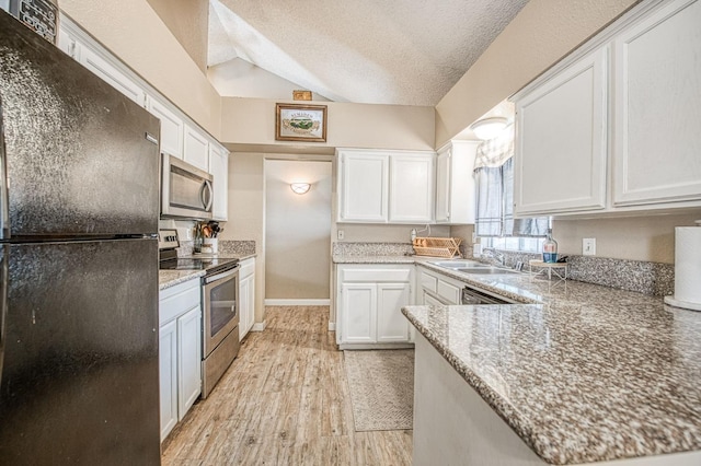 kitchen featuring white cabinets, a sink, light wood-style floors, stainless steel appliances, and vaulted ceiling