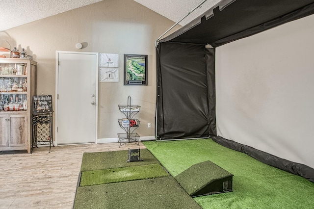workout room featuring a textured ceiling, golf simulator, wood finished floors, and lofted ceiling