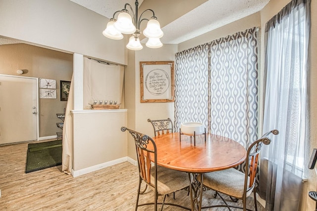 dining area featuring light wood-style floors, a textured ceiling, baseboards, and an inviting chandelier