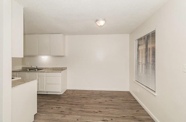 kitchen featuring a textured ceiling, wood finished floors, a sink, baseboards, and white cabinetry