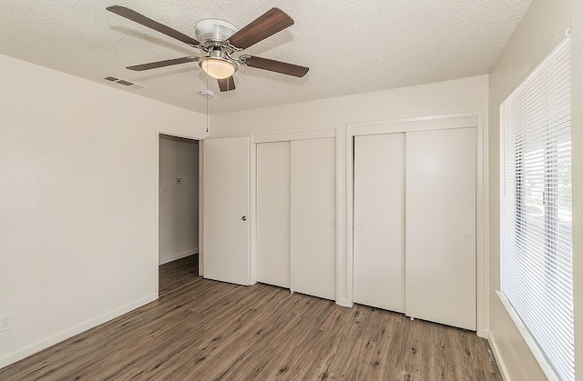 unfurnished bedroom with multiple closets, a textured ceiling, wood finished floors, and visible vents
