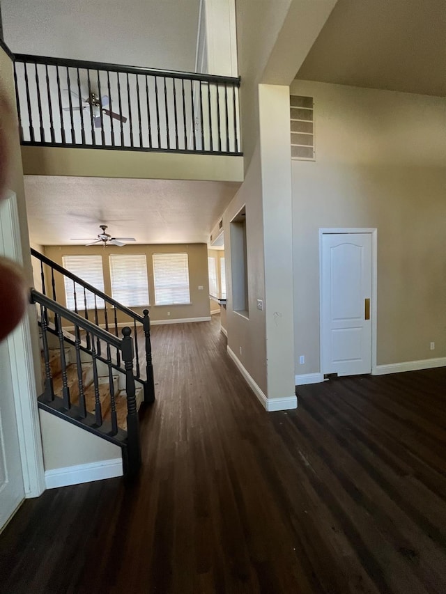 stairs featuring ceiling fan, baseboards, wood finished floors, a towering ceiling, and visible vents