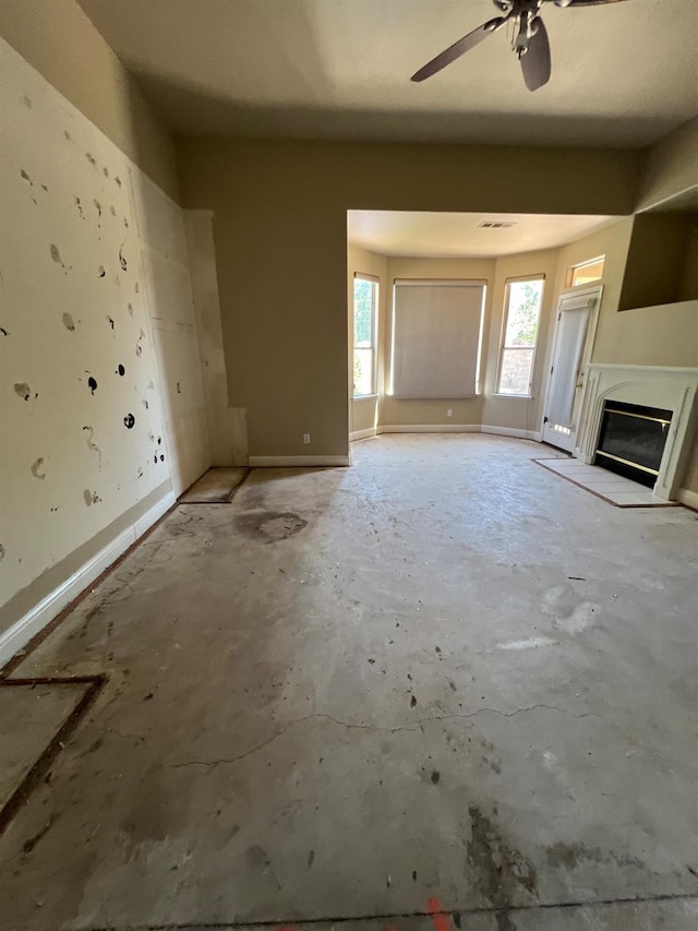 unfurnished living room with a ceiling fan, a glass covered fireplace, and unfinished concrete flooring