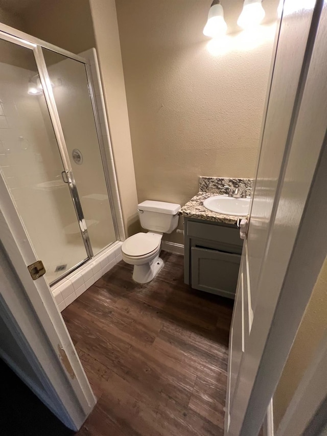bathroom featuring vanity, a textured wall, wood finished floors, toilet, and a stall shower