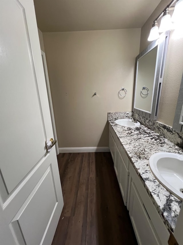 bathroom featuring double vanity, baseboards, a sink, and wood finished floors