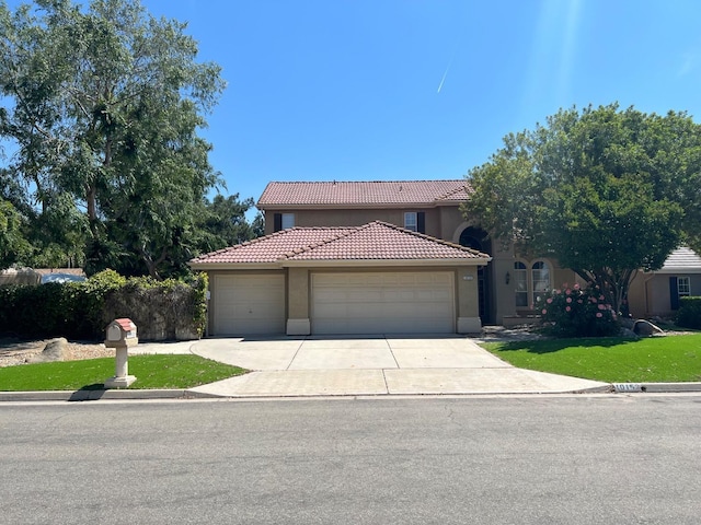 mediterranean / spanish-style home with a tile roof, a front yard, concrete driveway, an attached garage, and stucco siding