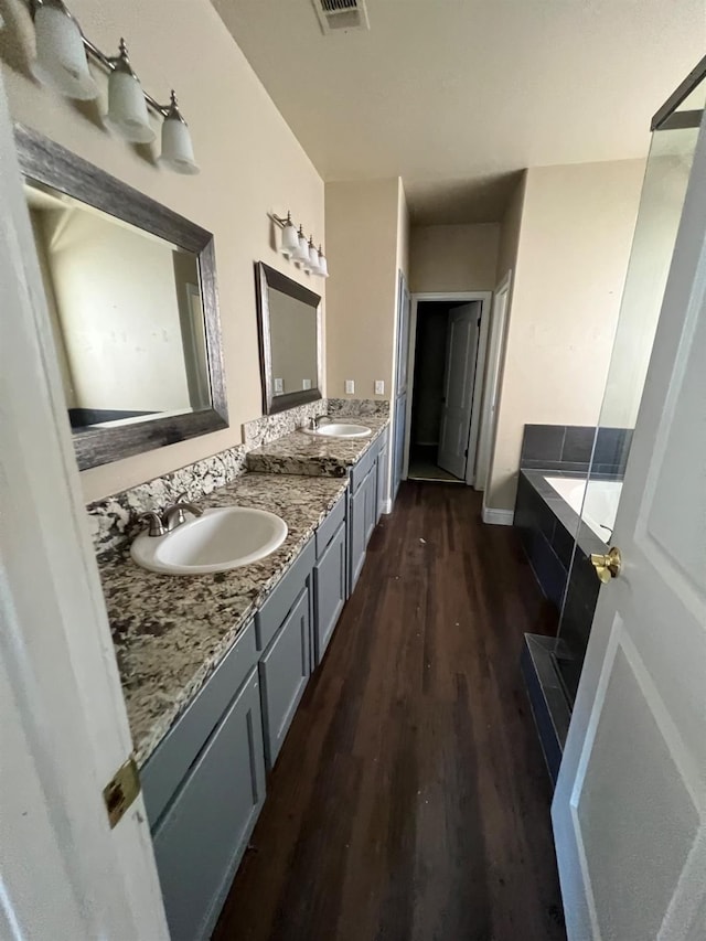 bathroom featuring double vanity, a garden tub, visible vents, wood finished floors, and a sink