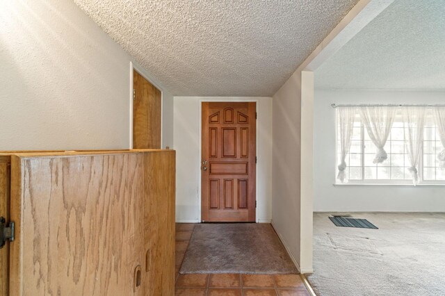carpeted foyer entrance featuring tile patterned flooring and a textured ceiling