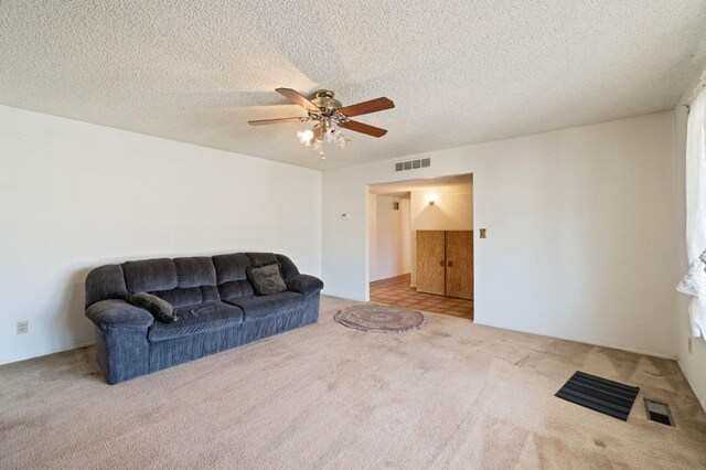 living room featuring carpet floors, a ceiling fan, a textured ceiling, and visible vents