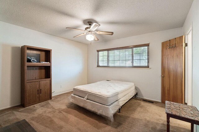 bedroom featuring visible vents, baseboards, ceiling fan, light colored carpet, and a textured ceiling